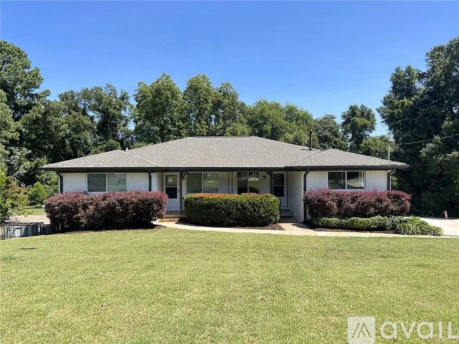 A house with a grey roof and white walls is surrounded by greenery.