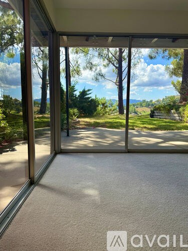A room with a carpet floor and glass doors leading to a garden.