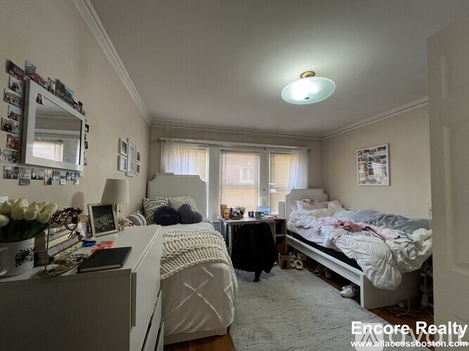 A bedroom with two beds, one with a white comforter and the other with a black comforter, a dresser with a mirror, and a window with curtains.