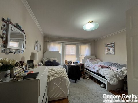 A bedroom with two beds, one with a white comforter and the other with a black comforter, a dresser with a mirror, and a window with curtains.