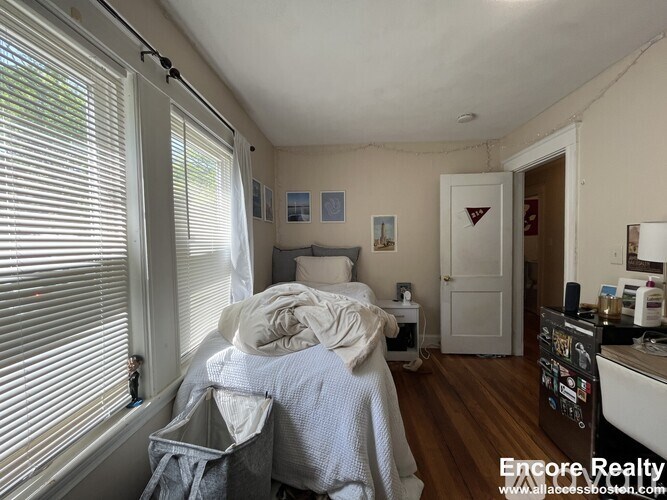 A bedroom with a bed covered in a blue blanket and a white door in the background.