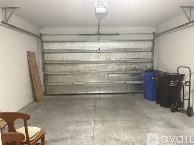 A large empty garage with a blue trash bin and a wooden chair.