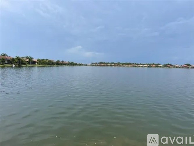 A body of water with a line of trees and buildings in the distance under a blue sky.