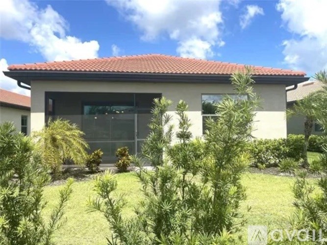 A house with a red tile roof and a large glass window is surrounded by greenery.