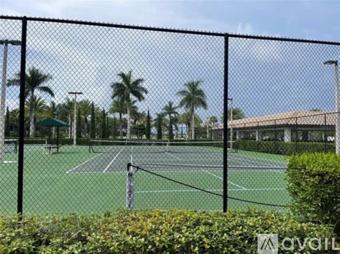 A tennis court surrounded by a black fence and greenery.