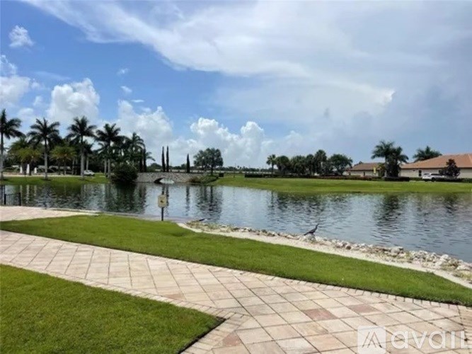 A walkway leads to a body of water with a bird on the grass.