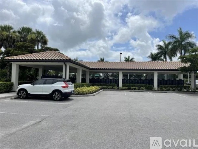 A white car is parked in a parking lot in front of a building with a tiled roof.