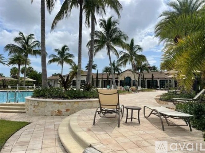 A poolside patio with chairs and a table surrounded by palm trees.