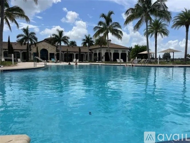 A large swimming pool surrounded by palm trees and a building in the background.