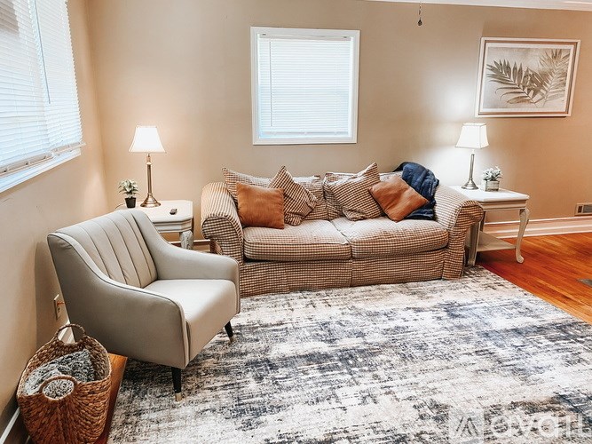 A living room with a beige sofa, a matching armchair, and a patterned rug.