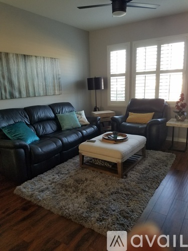 A living room with a black leather couch and a white ottoman.