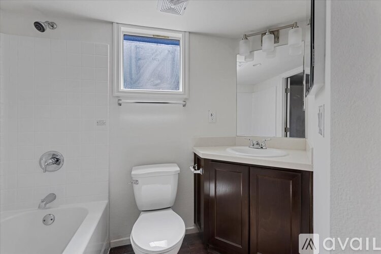 A white toilet sits in a bathroom with a white tub and brown cabinet.