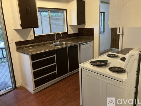 A kitchen with a white stove top oven and a sink with a window above it.