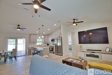 A modern living room with a large television and a kitchen area in the background.