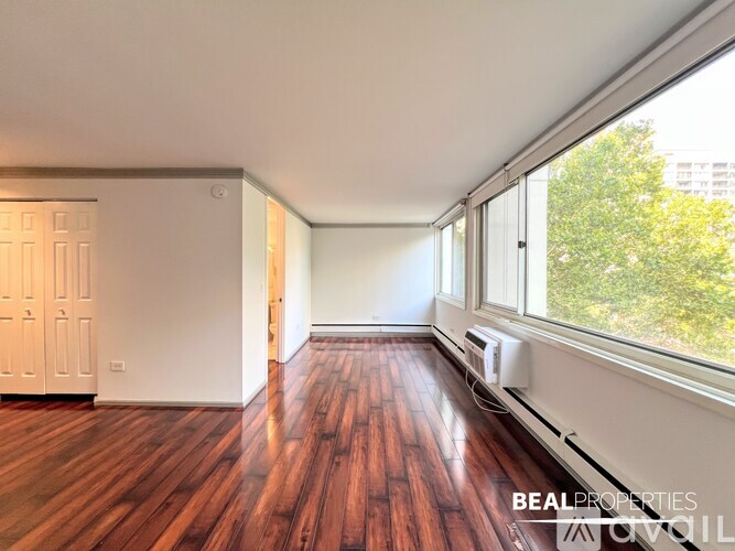 A spacious room with wooden flooring and white walls, with a kitchen area visible in the background.