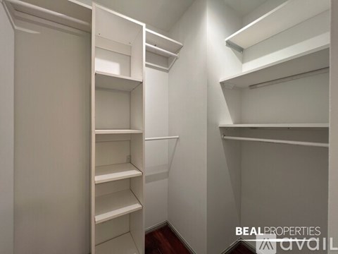 A spacious room with wooden flooring and white walls, leading to a kitchen area.
