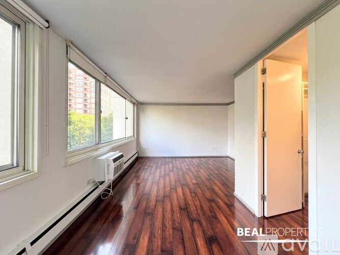 A room with wooden floors and white walls, with a window on the left and a door on the right.
