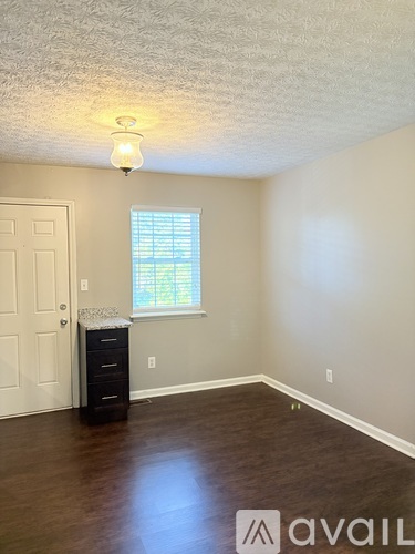 A room with a white door, a window with blinds, a dresser, and a ceiling light.