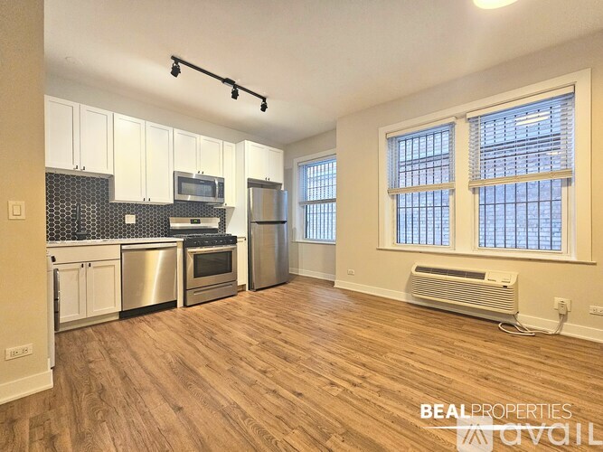 A spacious kitchen with wooden flooring and a window with blinds.