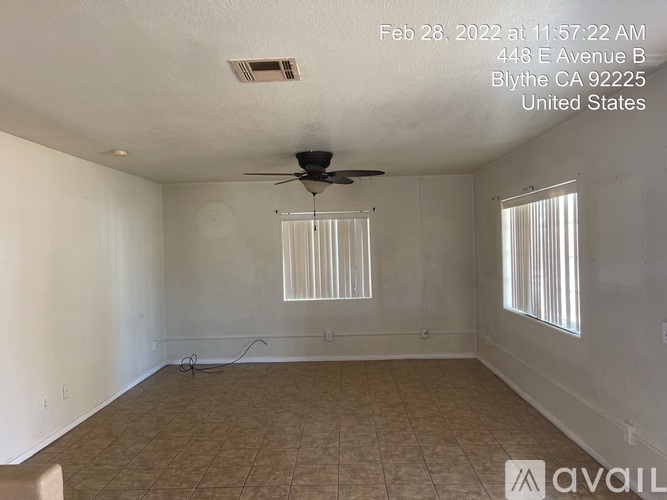 Empty room with a ceiling fan and two windows.