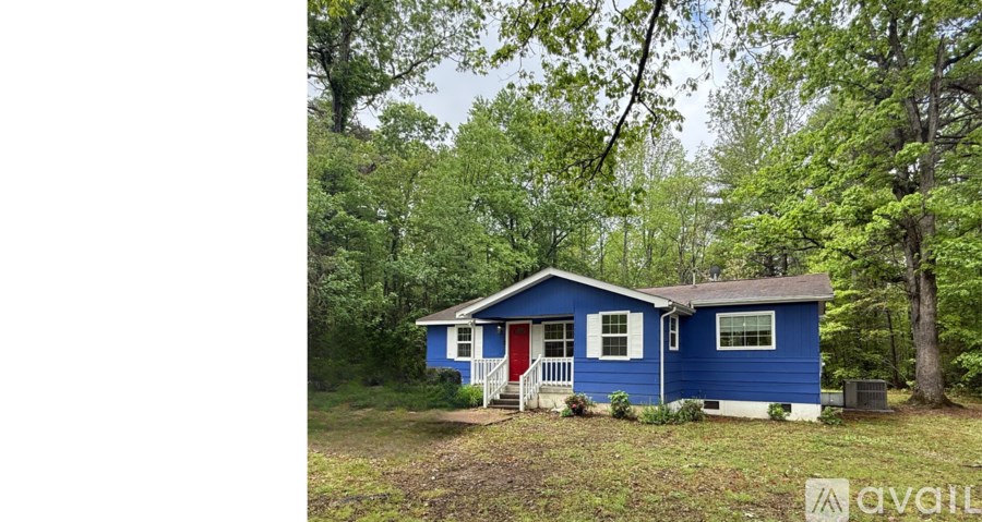 A blue house with a red door is surrounded by trees.