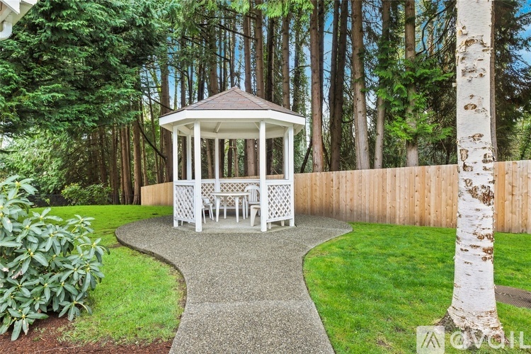 A gazebo with white railings is surrounded by a wooden fence and a gravel path.