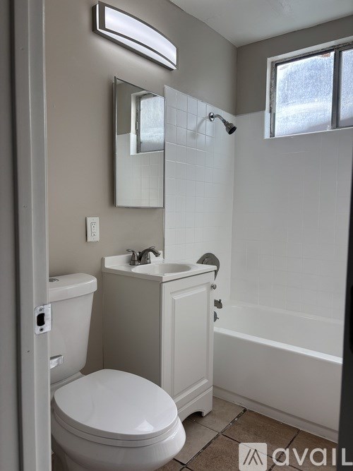 A white toilet is in a bathroom with a white sink and a mirror.