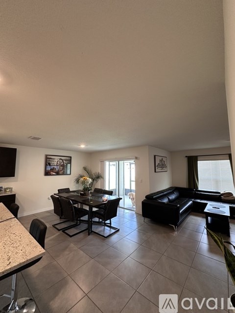 A living room with a black couch and a dining table with chairs.
