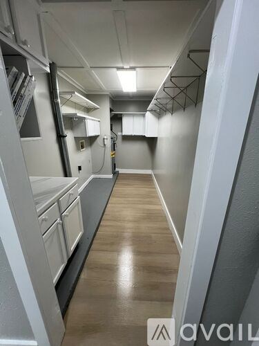 A long, narrow kitchen with white cabinets and a wooden floor.