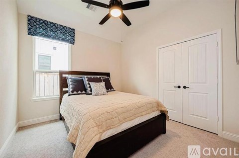 A bedroom with a bed, a window with a curtain, a ceiling fan, and a carpeted floor.