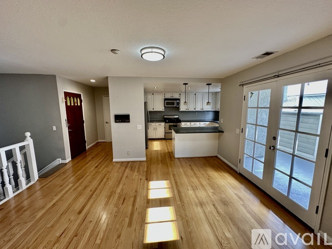 A spacious room with wooden flooring and a kitchen area in the background.