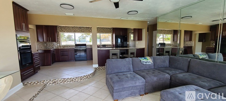 A spacious living room with a grey couch and a kitchen area with brown cabinets.