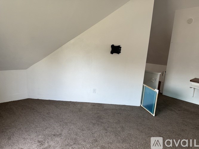 A room with a grey carpet and a white wall with a black object on it.