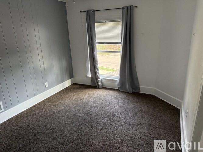A room with grey carpet and a window with grey curtains.