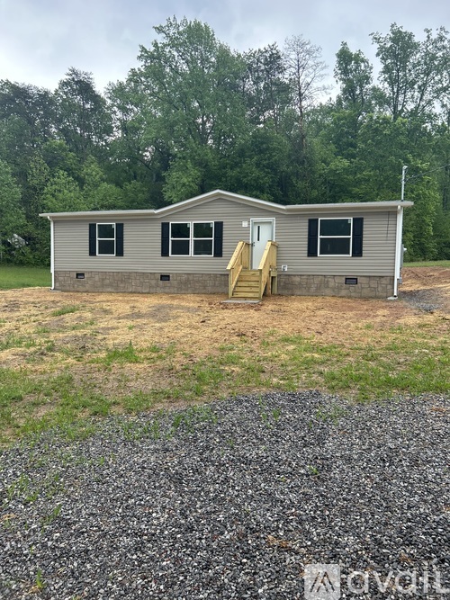 A small house with a brown roof and a grey siding is surrounded by trees.