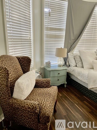 A leopard print chair with a white pillow sits in front of a window with blinds.