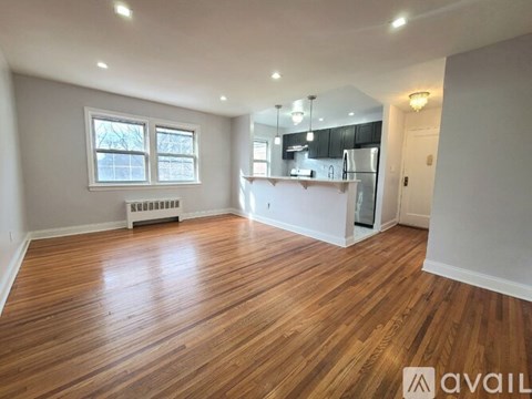 A spacious room with wooden flooring and a kitchen area in the background.