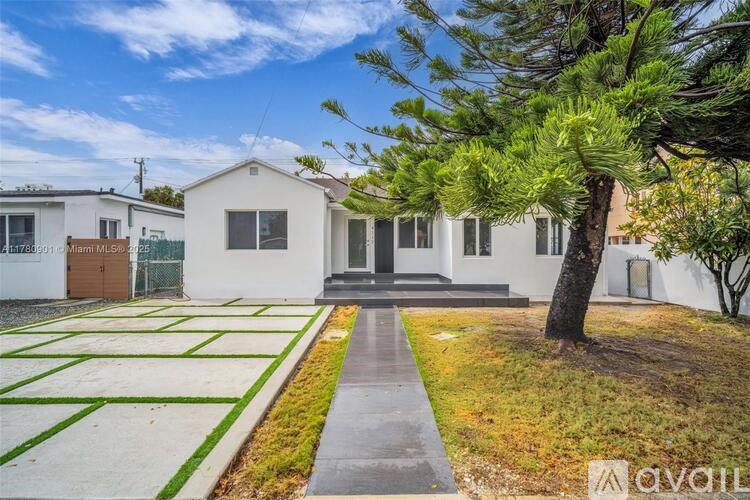 A white house with a tree in front and a fence behind it.