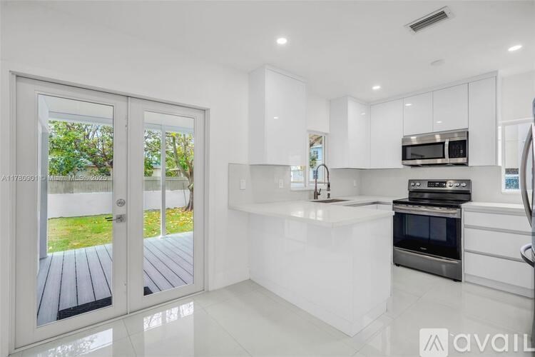 A modern kitchen with white cabinets and appliances, a large island, and a view of a deck through the sliding glass doors.