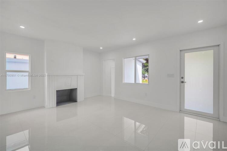 A spacious, white room with a fireplace and a large window.