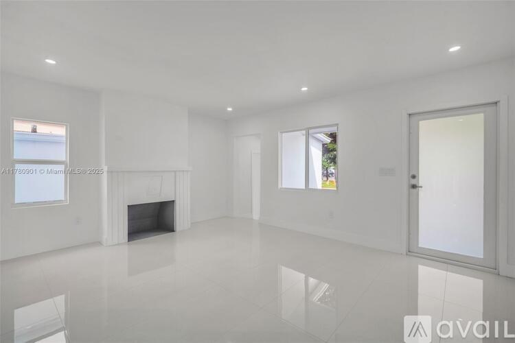 A spacious, white room with a fireplace and a large window.