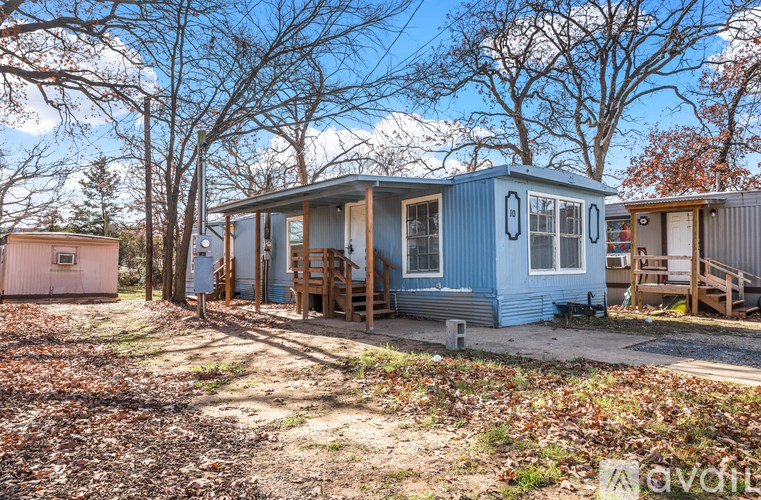 A blue house with a brown door and windows is surrounded by trees.
