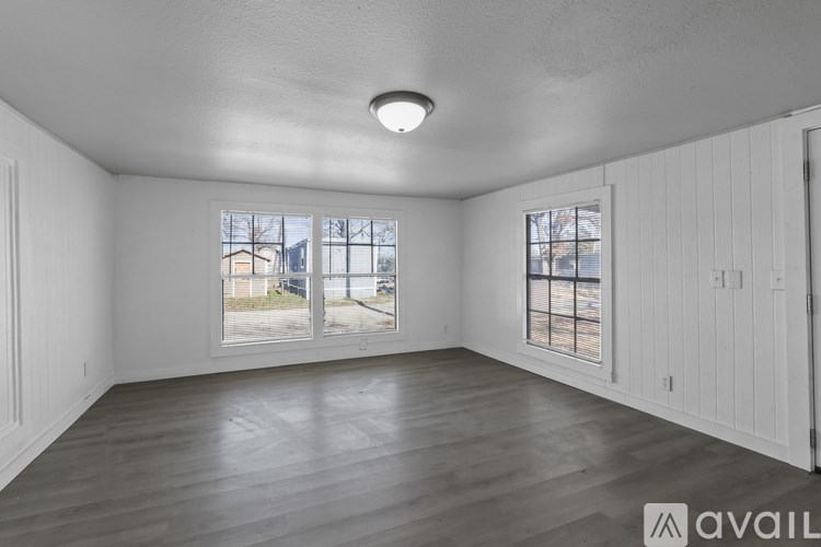 A room with wooden flooring and two windows overlooking a street.