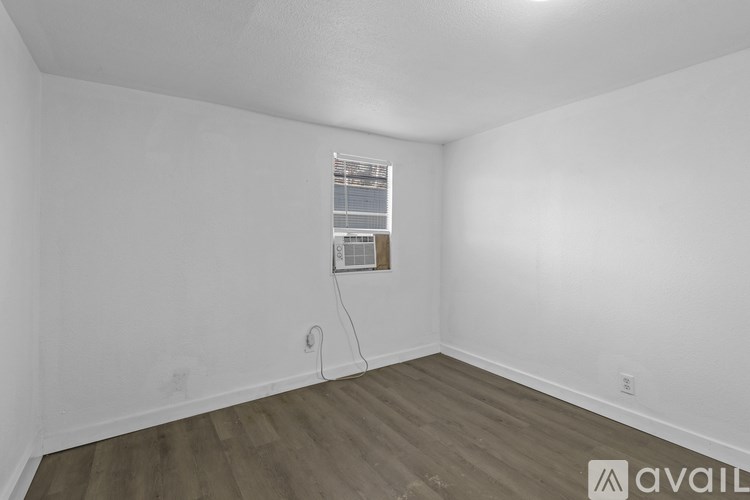 Empty room with wooden flooring and a window with blinds.