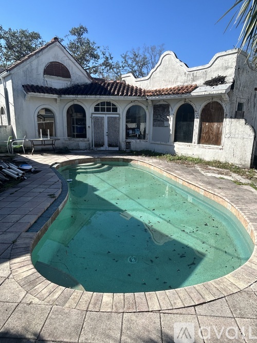 A pool in front of a white building with a tiled roof.
