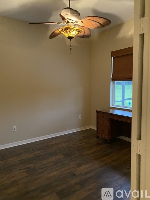 A room with a ceiling fan and a desk with a window.