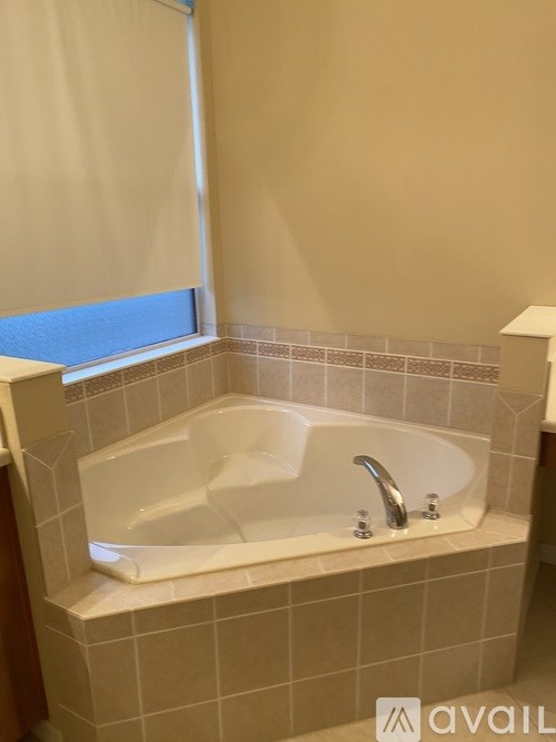 A white bathtub with a silver faucet is in a bathroom with beige walls.