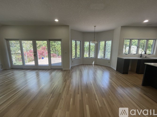 A spacious room with wooden flooring and large windows.