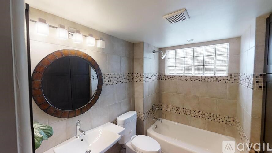 A bathroom with a round mirror, sink, toilet, and bathtub.