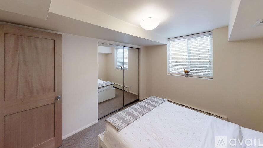 A bedroom with a bed, a window with blinds, and a wooden door.